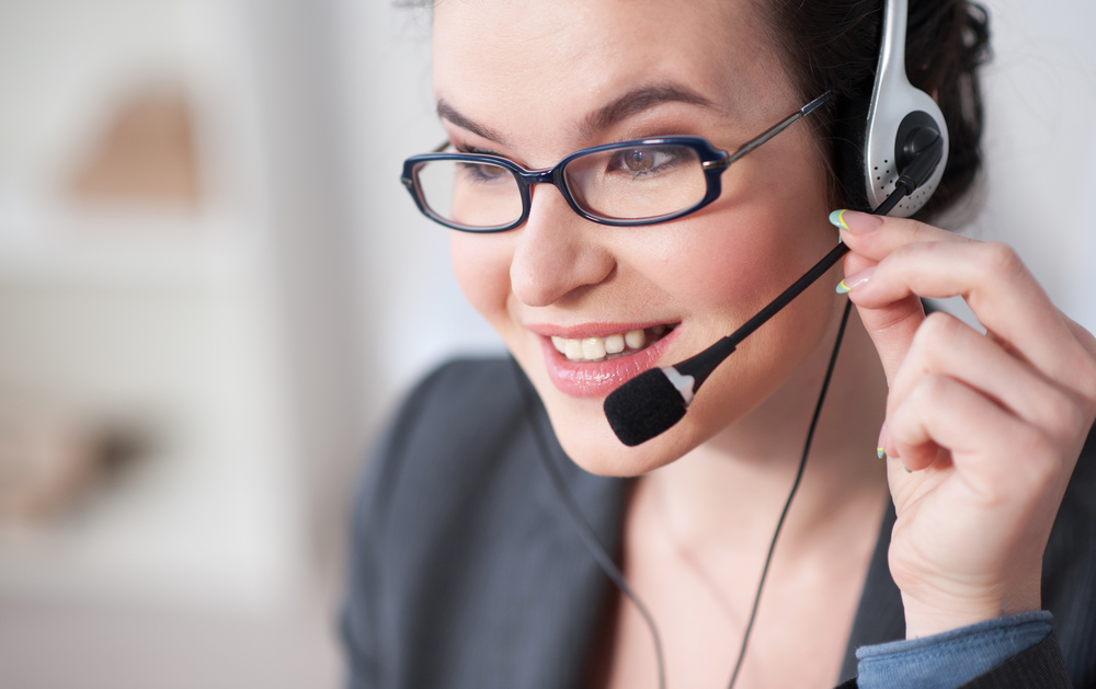 I am listening to you. Pretty female operator is working with headset. She is touching the microphone and smiling