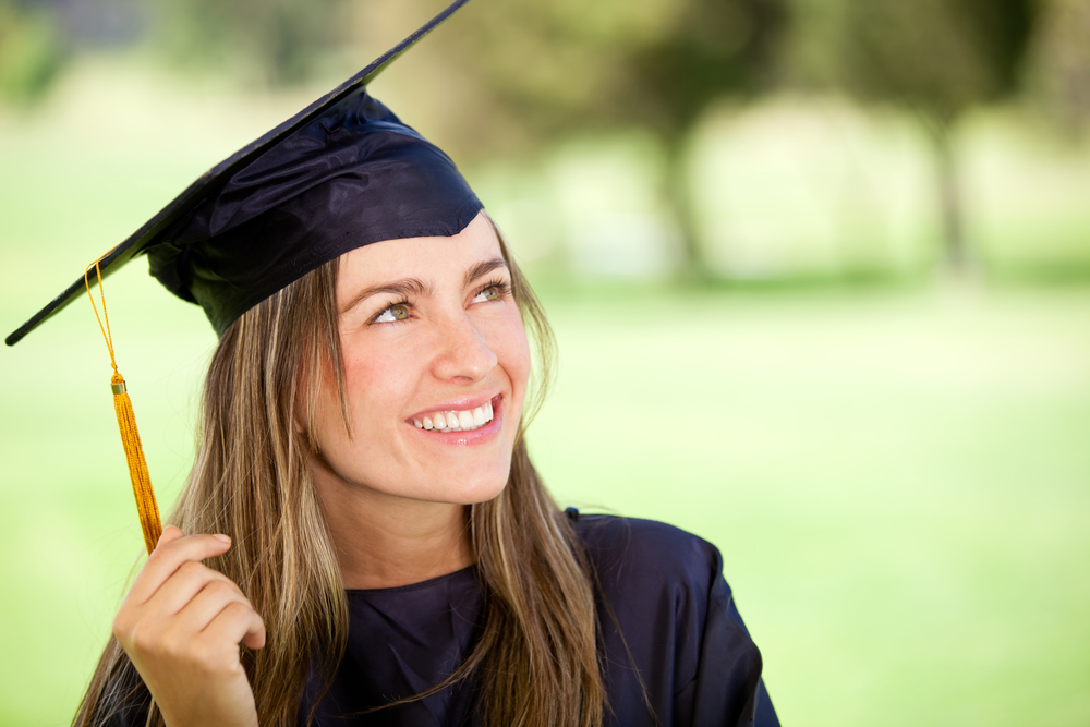 Pensive graduation student looking up outdoors and smiling