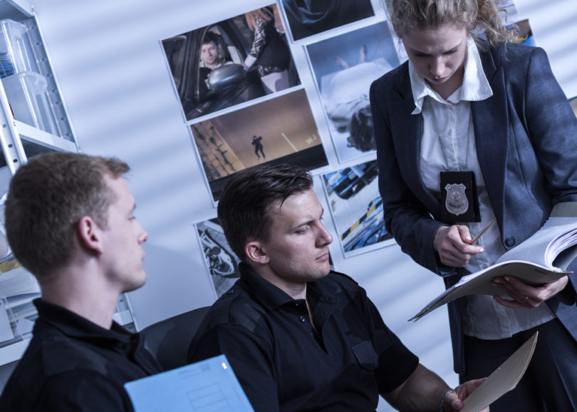 Two police officers and female detective working at a police station, analyzing evidences