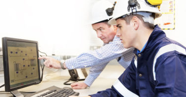 Senior and junior engineers discussing work together in office, senior man pointing at screen