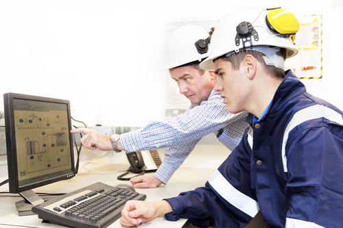 Senior and junior engineers discussing work together in office, senior man pointing at screen