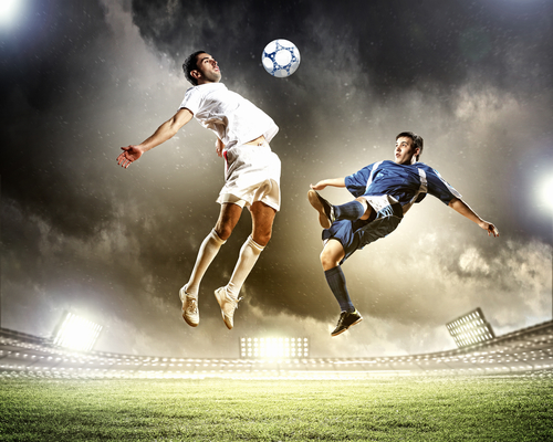 two football players in jump to strike the ball at the stadium