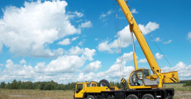 Yellow automobile crane with risen telescopic boom outdoors over blue sky