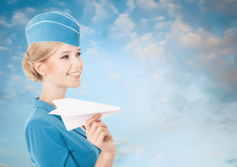 Charming Stewardess Holding Paper Plane In Hand. Blue Sky Background.