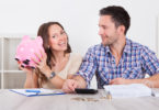 Young Man Looking At Woman Inserting Coin In Piggybank