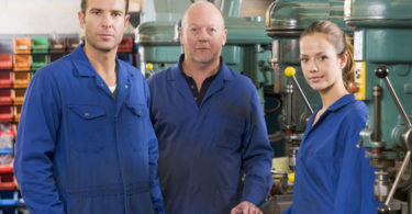 Three machinists in workspace by machine talking