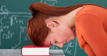 Side view of sad young female student leaning head on book in classroom