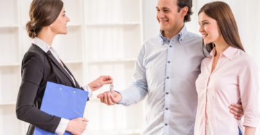 Female realtor is giving to young couple a key from new flat.