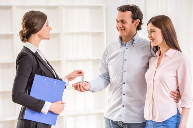 Female realtor is giving to young couple a key from new flat.