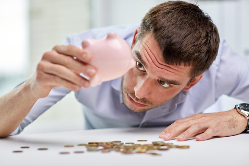 business, people, finances, crisis and money saving concept - businessman shaking piggy bank and getting coins at office