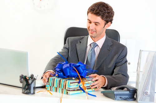 Pleased modern businessman sitting at office desk and looking on gift