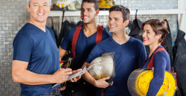 Portrait of happy fireman standing with team at fire station