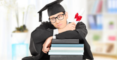 Worried college graduate leaning on a stack of books, indoors