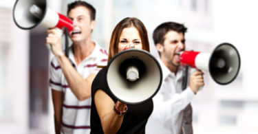 portrait of a angry  group of employees shouting using megaphones against a city background