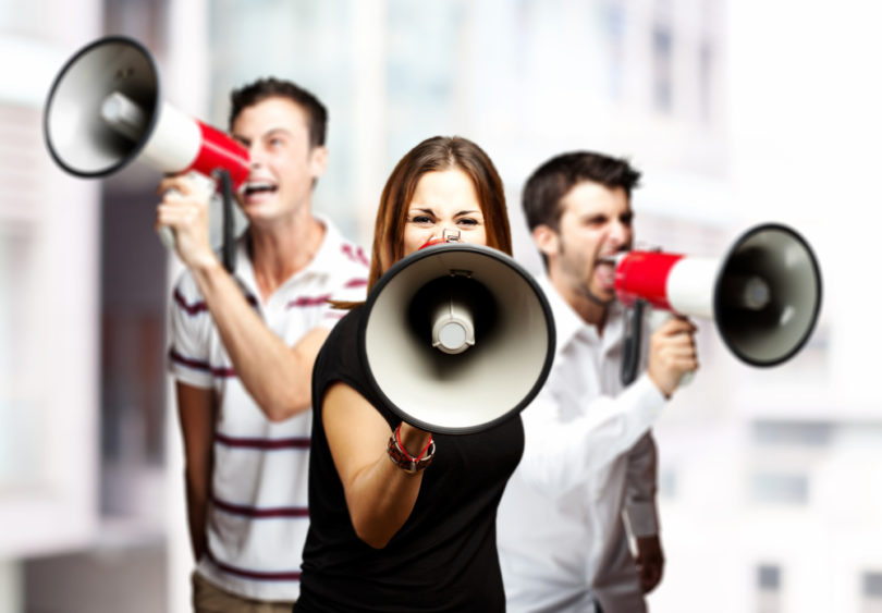 portrait of a angry  group of employees shouting using megaphones against a city background