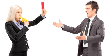 Woman in business suit showing a red card and blowing a whistle to a man in a business suit, isolated on white background