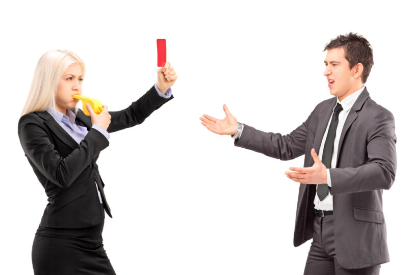 Woman in business suit showing a red card and blowing a whistle to a man in a business suit, isolated on white background