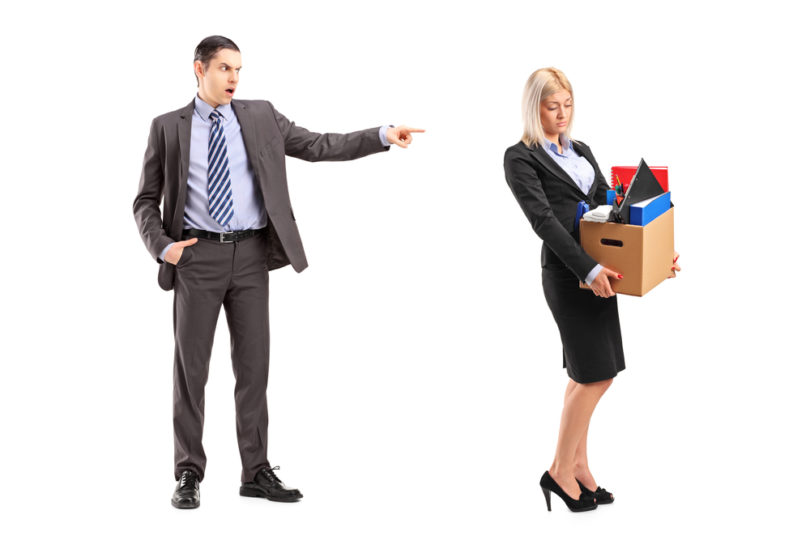 Full length portrait of an angry boss firing a woman with a box of her personal items isolated on white background