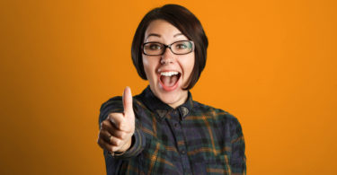 Cheerful young woman showing thumb up sign on orange background