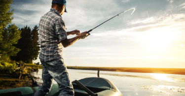 Mature man fishing from the boat on the pond at sunset