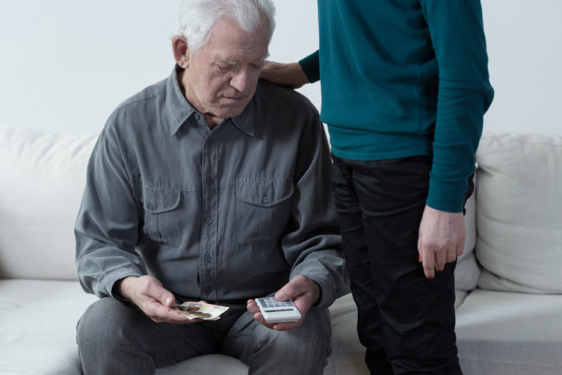 Poor senior man using calculator and counting money