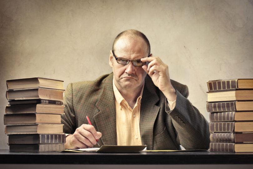 Severe teacher at his desk surrounded by books and paper sheets