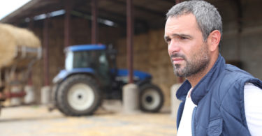 Farmer standing in front of a barn containing a tractor