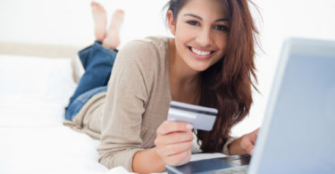 A woman smiling and looking in front of her as she uses her credit card with her laptop.