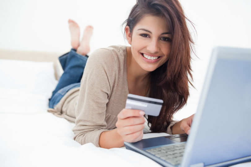 A woman smiling and looking in front of her as she uses her credit card with her laptop.