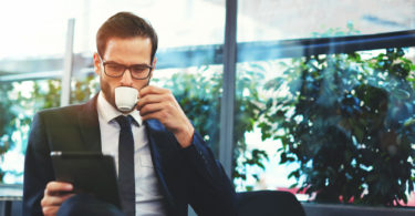 Portrait of handsome successful man drink coffee and look to the digital tablet screen sitting in coffee shop, business man having breakfast sitting on beautiful terrace with plants