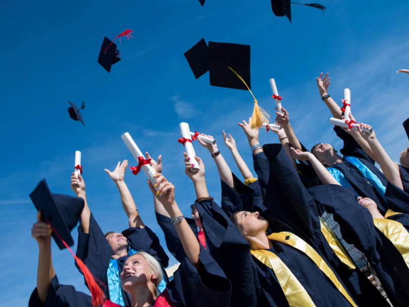 high school students graduates tossing up hats over blue sky.