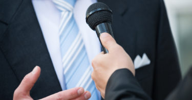 Midsection of male journalist taking interview of businessman outdoors