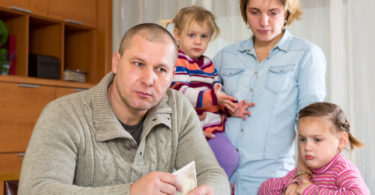 Family having problems with cash. Father is sitting at the table with money in his hands his wife and two sad daughters are sitting behind him